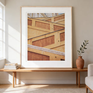 a large framed photograph of a building with a wooden frame, hanging on a wall above a wooden table with a stack of books and a vase of greenery.