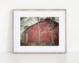 Rustic red barn with stone foundation and bare winter trees, photographed in a rural countryside setting
