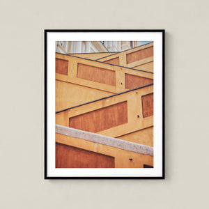 The image is a framed photograph of a building with a geometric pattern of wooden panels and a concrete surface.